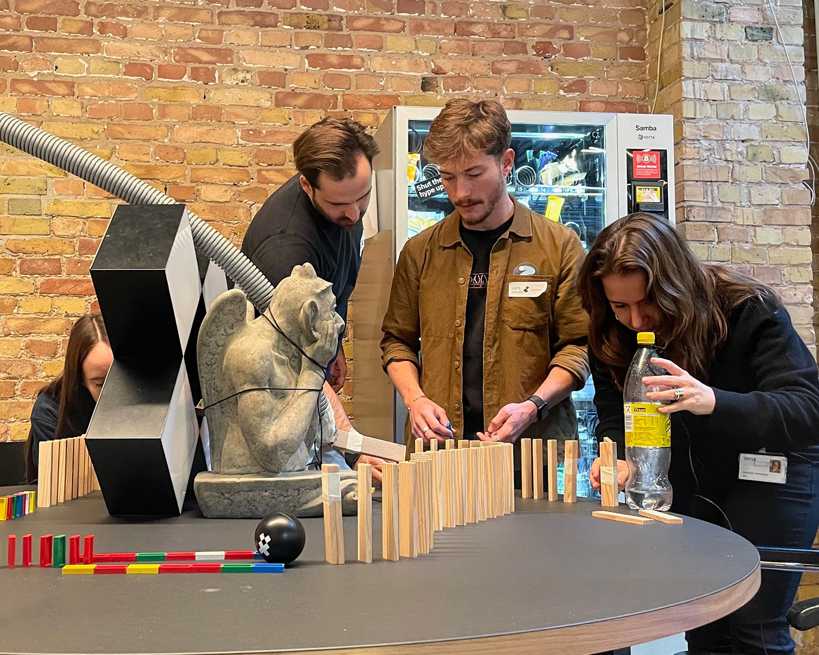 Drei Personen bauen im Büro eine Rube-Goldberg-Maschine