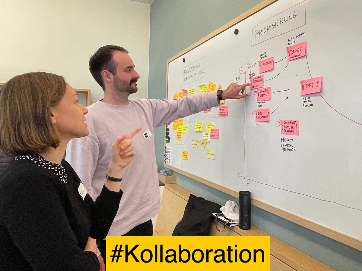 Two people looking at whiteboard with sticky notes, hashtag collaboration