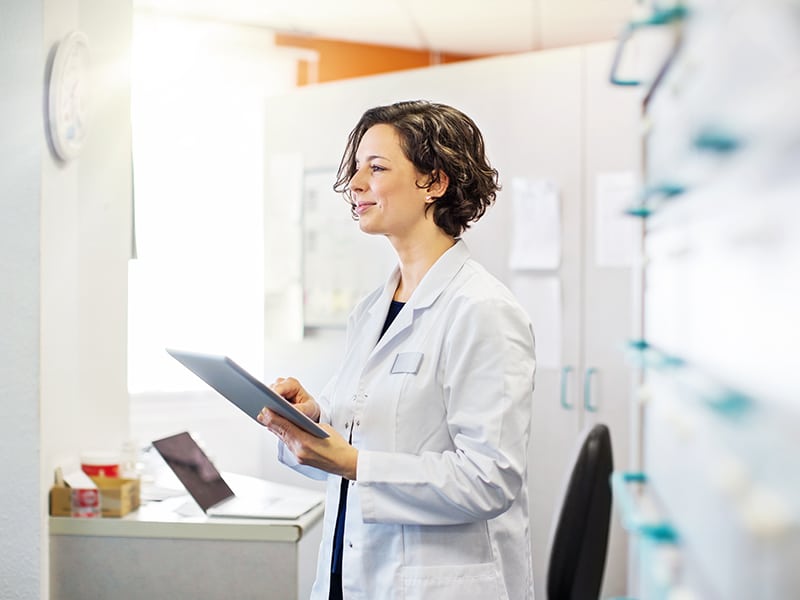 Woman in lab coat holding a tablet.