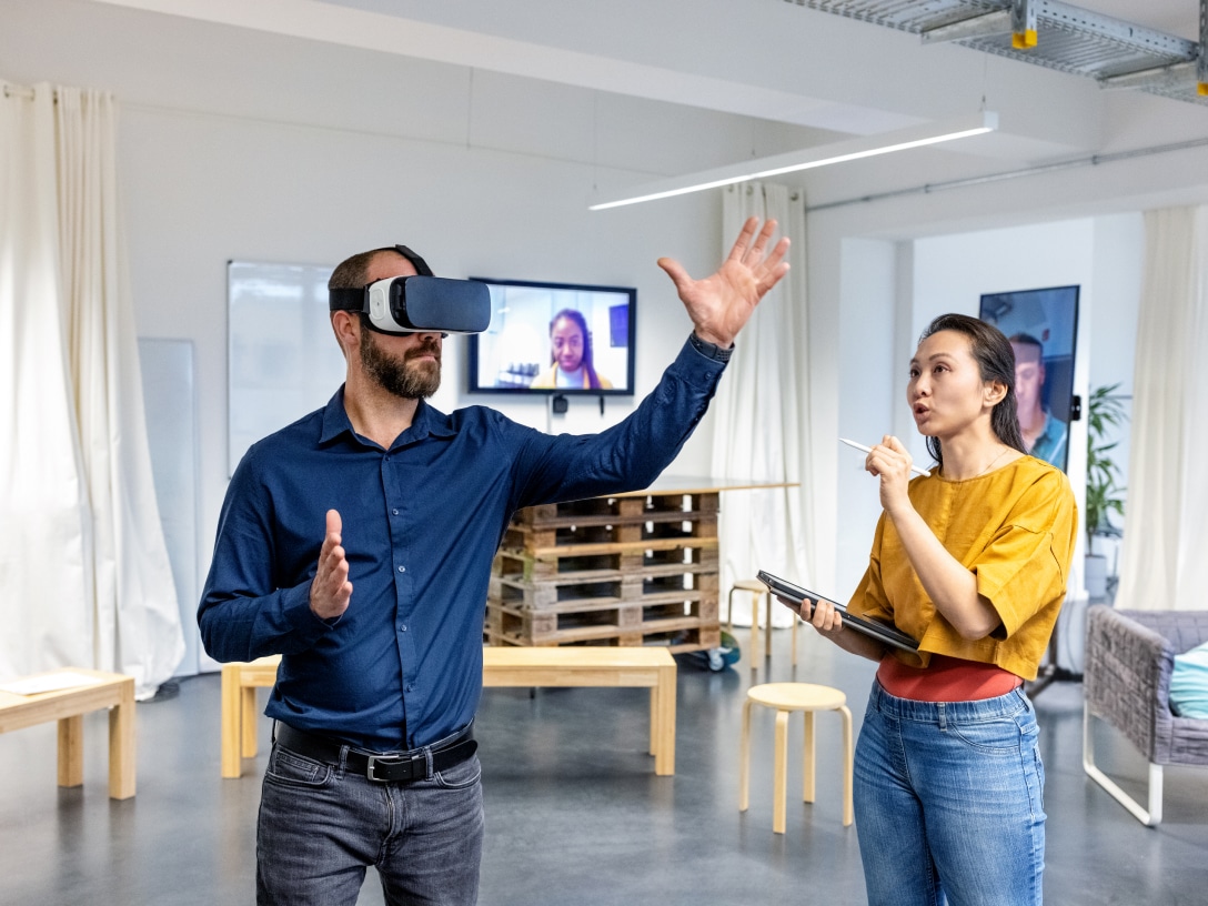 Person mit VR-Brille steht in einem Raum und weitere Person spricht mit ihr