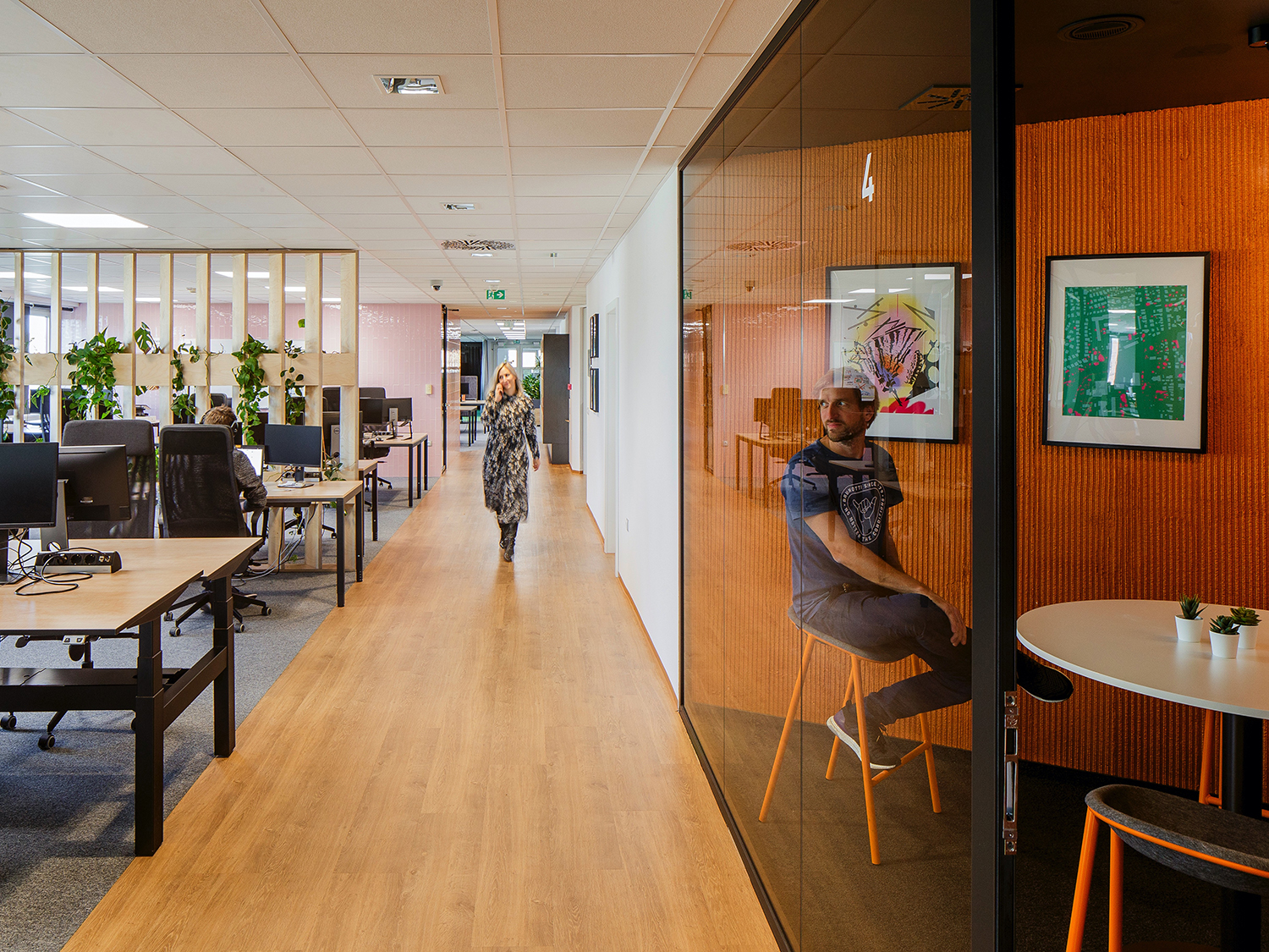 Open office space with wooden floors and an ajoining orange office behind a glass wall.