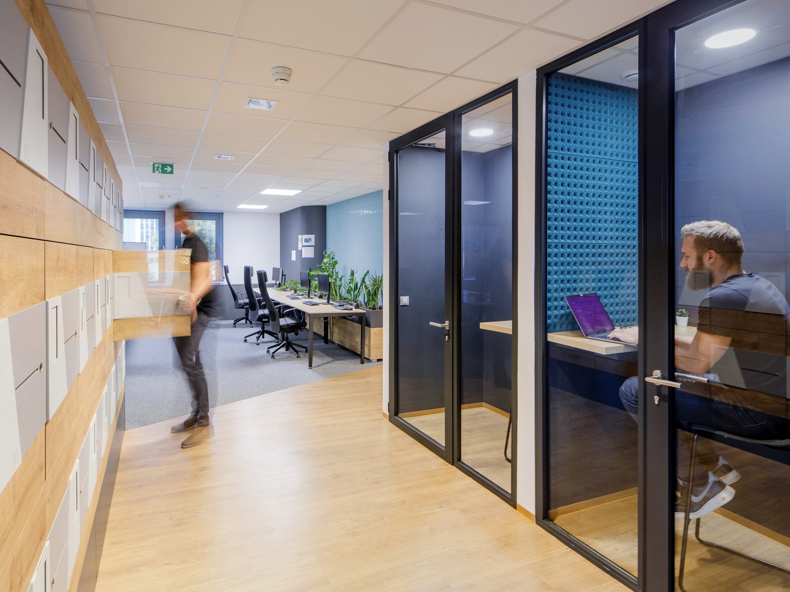 Open office space with wooden floors and an ajoining blue office behind a glass wall.