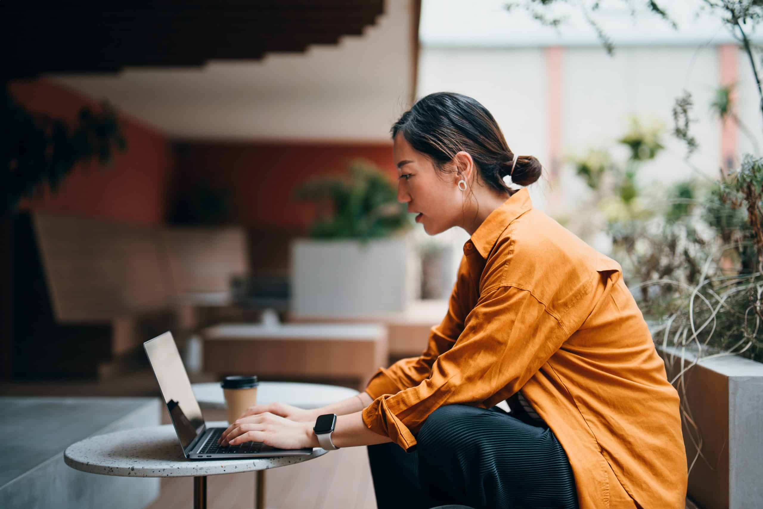 Confident young Asian businesswoman working on laptop with business clients in outdoors co-working space, surrounded by green plants. Remote working. Working outdoors with technology. Staying connected to her business. Lifestyle. Business or leisure theme