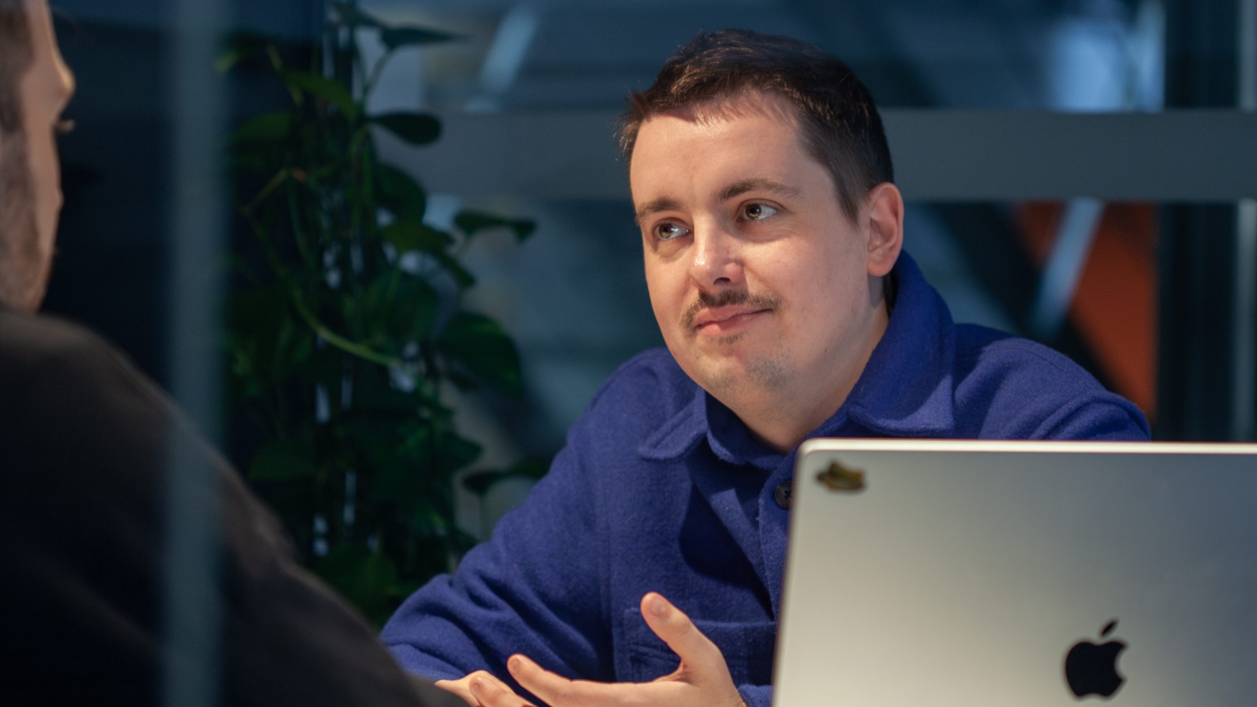 UI Designer Erik Lorenz is sitting at his laptop, talking to a colleague