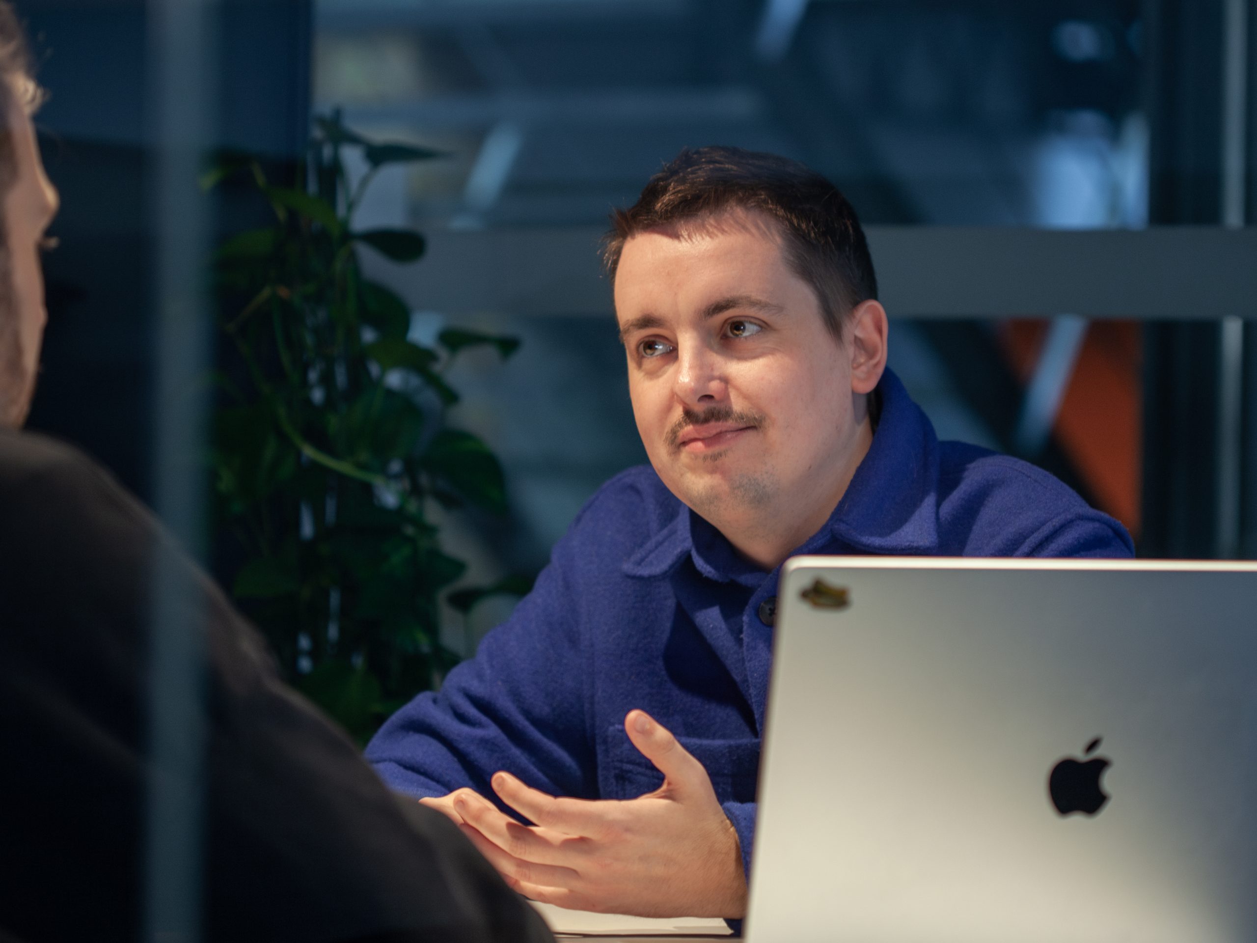 UI Designer Erik Lorenz is sitting at his laptop, talking to a colleague