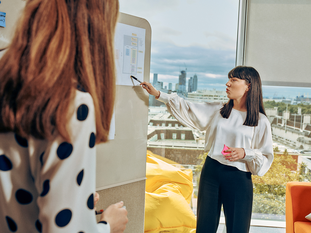 Zwei Frauen diskutieren über ein Diagramm auf dem Whiteboard.