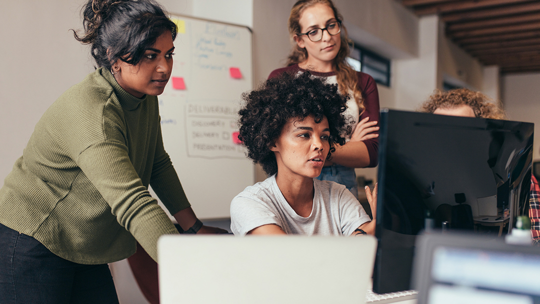 Gruppe von Menschen, die in einem Büro zusammenarbeiten, versammelt um einen Tisch mit Computern und Laptops.
