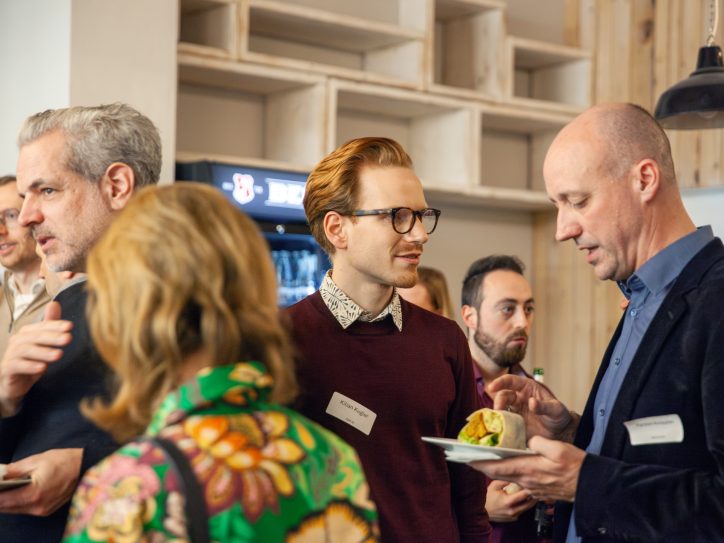 Eine Gruppe von Menschen vernetzt sich bei einer Veranstaltung, trägt Namensschilder und genießt Essen.
