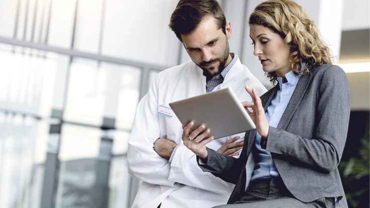 Scientist and businesswoman discussing data on a tablet in a hallway