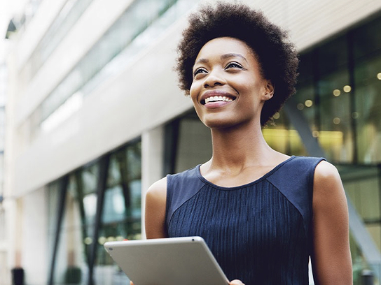 Smiling woman standing outside a building, holding tablet.