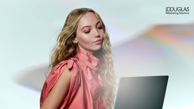 Junge Frau mit langen blonden Haaren und natürlichem Make-up arbeitet an einem Laptop – modernes digitales Marketing Konzep