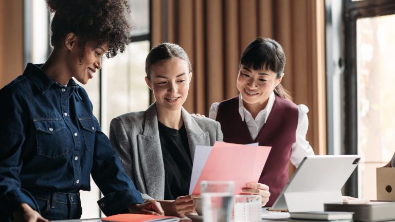 team collaborating on customer experience transformation project, featuring three professionals reviewing documents in a modern office setting.