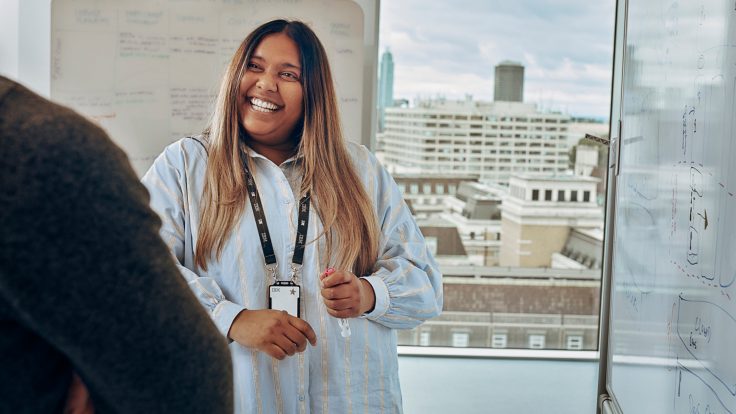 Teammitglied präsentiert Konzepte für personalisiertes Marketing an einem Whiteboard in einem Büro mit Stadtblick.