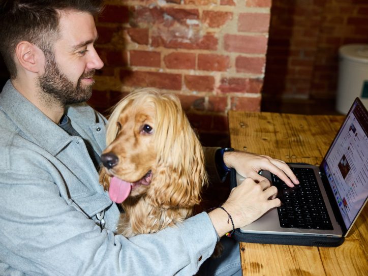 Ein Mann sitzt mit einem Hund vor einem Laptop.
