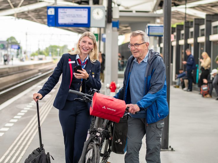 Bahnmitarbeitende unterstützen Reisenden mit Fahrrad am Bahnsteig mithilfe einer mobilen App und zeigen digitale Omni-Channel Customer Experience im öffentlichen Verkehr.