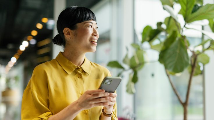 Frau mit Smartphone nutzt digitalen Kundenservice eines Energieversorgers in modernem Büro – Symbol für kundenorientierte Services im Energiesektor